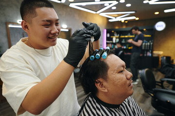 Smiling barber putting rollers in wet hair of client