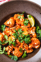 Baked cauliflower in tomato sauce with herbs, white background.