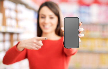 Cheerful woman showing a smartphone at the supermarket