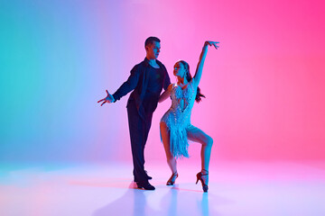 Duet of ballroom dancers, man and woman, in stage costumes posing in neon lighting against gradient...