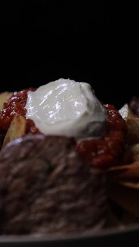 Closeup vertical footage of adding the fresh basil to garnish the Iskender Kebab plate