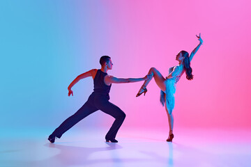 Man and woman, ballroom dancers, performing full of feelings tango dance in neon lighting against...