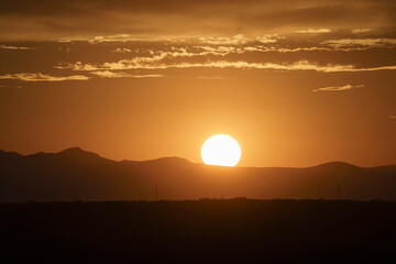 The sun is setting over a mountain range, casting a warm glow over the landscape.
