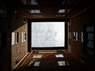 View of the cloud-covered sky from inside the courtyard of a square building surrounded by windows