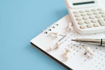 Close up of ball pen on white calendar with blurred thumbtack and calculator