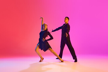 Ballroom dancers, man and woman in stage costumes gracefully performing in neon lighting against...