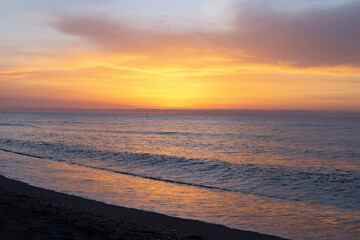 A beach sunrise with clouds in vibrant colors reflecting off the sea, creating a perfect sunset.