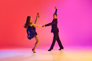 Professional ballroom dancers in black stages costumes performing in neon lighting against vibrant gradient background. Concept of dance and music, sport, action, competition, classical. Ad