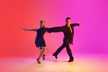 Pair of ballroom dancers showcasing their moves in neon lighting against vibrant gradient background. Talented artists. Concept of dance and music, professional sport, action, competition, classical.