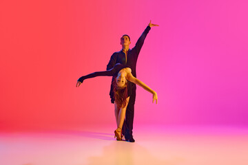 Duet of ballroom dancers, man and woman, in stage costumes posing in neon lighting against vibrant...