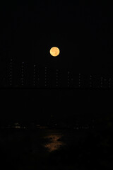 Full moon over Bosphorus bridge at night in Istanbul. The bright and full moon dominates the sky. Perfect for themes related to astronomy, lunar phases, and celestial events.