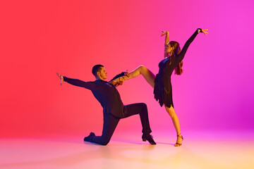 Man and woman, ballroom dancers, performing full of feelings tango dance in neon lighting against vibrant gradient background. Concept of music, professional sport, action, competition, classical. Ad