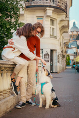 Young Caucasian couple sitting on curb and play with purebred dog Aussie. Vertical orientation. Pet...