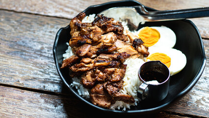 Grilled chicken and boiled eggs on rice are placed on a wooden table. ,grilled chicken on rice