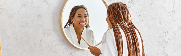 A woman with afro braids gazes at her reflection in a bathroom mirror, focusing on self-image and...