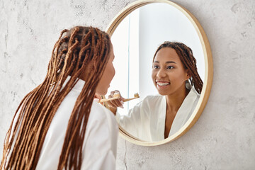 An African American woman with afro braids in a bath robe brushing her teeth in a modern bathroom...