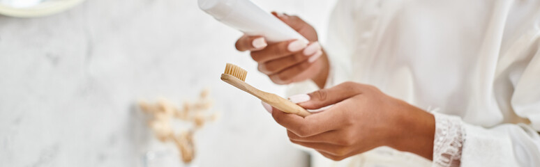 A close-up of an African American woman with Afro braids holding a toothbrush in her modern bathroom.