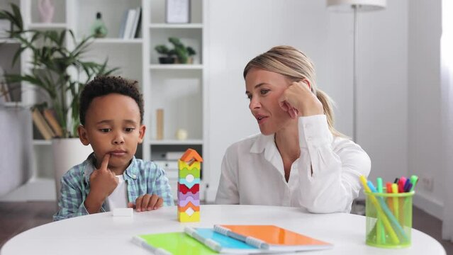 Assessment of mental development of children. Professional psychologist observes small multiracial boy playing with puzzle game, assessing his readiness for preschool. Exercises for kid with autism.