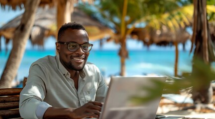 A happy black man in his thirties working on a laptop at a tropical beach bar, using the computer for remote work while vacationing at an exotic island resort with palm trees and blue ocean water.