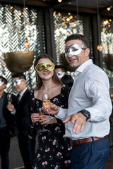couple of young lover toasting with clinking champagne glasses at funny and happy Christmas and new year mask party atmosphere. Holiday celebrate and nightlife lifestyle concept