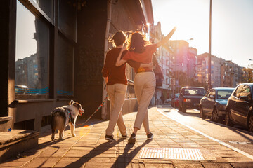 Back view of happy couple man and woman is walking around city with their dog. Sunset light in...
