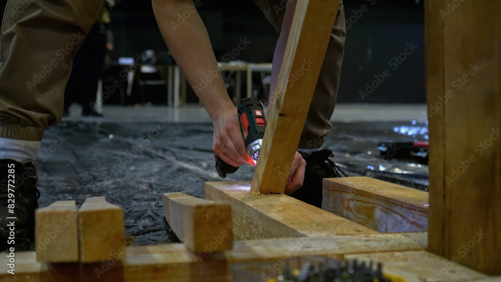 Poster carpenter working at workshop. media. worker using a screwdriver for assembling wooden construction.