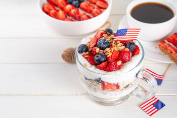 USA patriotic breakfast or brunch simple recipe idea, layered granola dessert, or overnight oatmeal in glass decorated with white whipped yogurt, blue and red berries and american flag