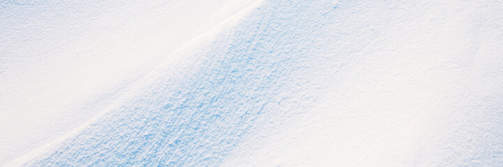 Beautiful winter background with snowy ground. Natural snow texture. Wind sculpted patterns on snow surface. Wide panoramic texture for background and design. Closeup top view with copy space.