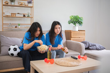 Asian women intently watching soccer game at home. Concept of sports, focus, and friendship