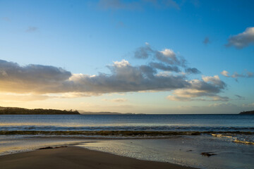 sunrise reflecting on the beach with golden light as waves roll in and water moves on the sand, calming waves