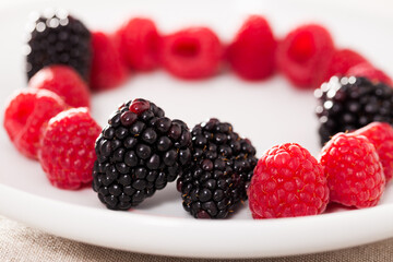 Raspberries and blackberries laid out on a white plate in circle