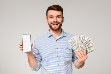 Freelance work. Handsome guy with cellphone with blank screen and fan of dollars on grey studio...