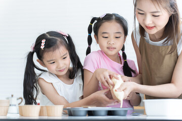 Asian family, mother and two daughters enjoy making cupcakes together at home kitchen. Mom and little child girl squeezing cake batter into cupcake paper cup, prepare for bake, smiling. Happy holiday