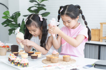 Asian two children enjoy making cupcakes together at home kitchen. Little cute child girls...