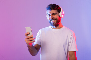 A man wearing headphones is holding a cell phone in his hand. He appears focused on the device,...
