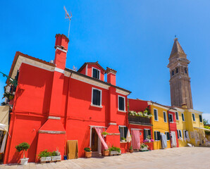 Colourful buildings with ancient spired church towering behind (Burano, Italy)