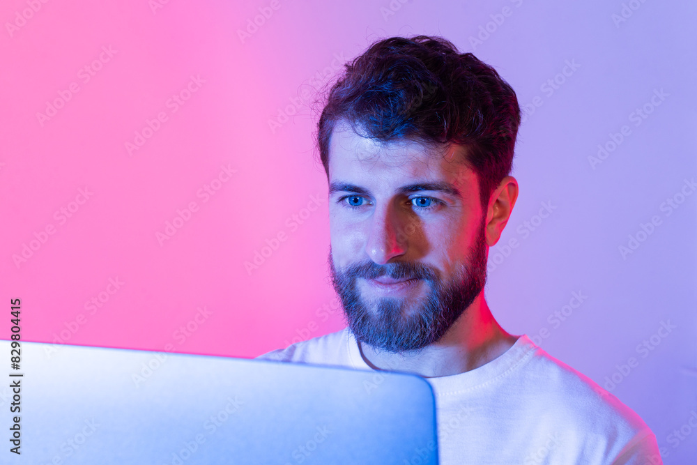 Poster A man with a beard sits in front of a laptop computer, typing and browsing the internet. He is focused on the screen, working or communicating online.