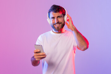 A man is shown wearing headphones and holding a cell phone in his hand. He appears to be listening...