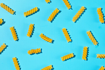 Uncooked fusilli pasta spirals scattered on a blue background in a decorative pattern