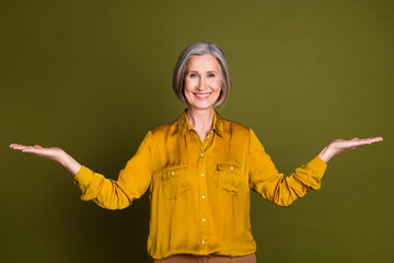Photo of good mood pretty lady dressed blouse comparing arms empty space isolated khaki color...