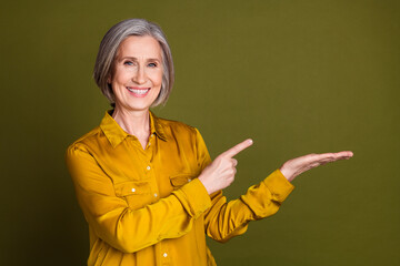 Photo of cheerful attractive lady dressed blouse showing arm pointing empty space isolated khaki...