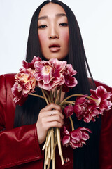 Woman with long black hair and red jacket holding pink tulips in a sunny garden setting