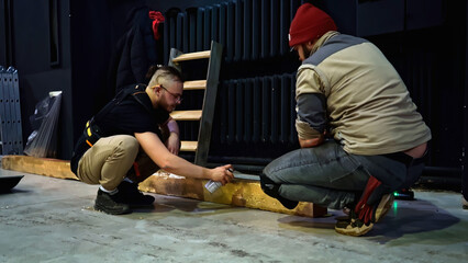 Spray painting of wooden beam in a concert hall. Media. Young man decorating wooden beam by black...