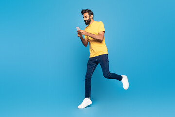 Fototapeta premium An adult Indian man wearing a yellow shirt is jogging outdoors with his attention focused on a smartphone screen.