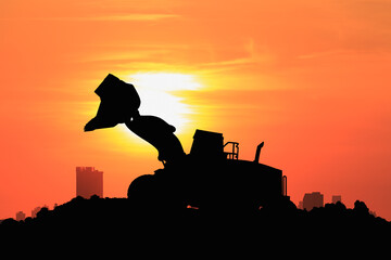 Wheel loader silhouette are digging the soil in the construction site on the  sunset background