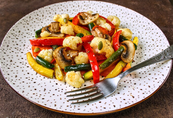 Fried vegetables with spices on a white plate. Vegetarian, diet food on a dark background.