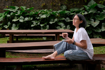 Woman enjoying her free time sitting on garden bench drinking a cup of hot chocolate