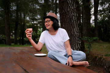 Woman admiring tasty hot chocolate she is having in her right hand, while sitting on garden bench