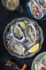 Oysters on a dish with ice, with lemon, lime, and white wine, overhead flat lay shot on a black slate background