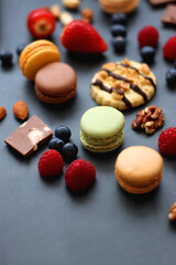 Macarons, chocolate, cookies, berries and various nuts on dark blue background. Selective focus.